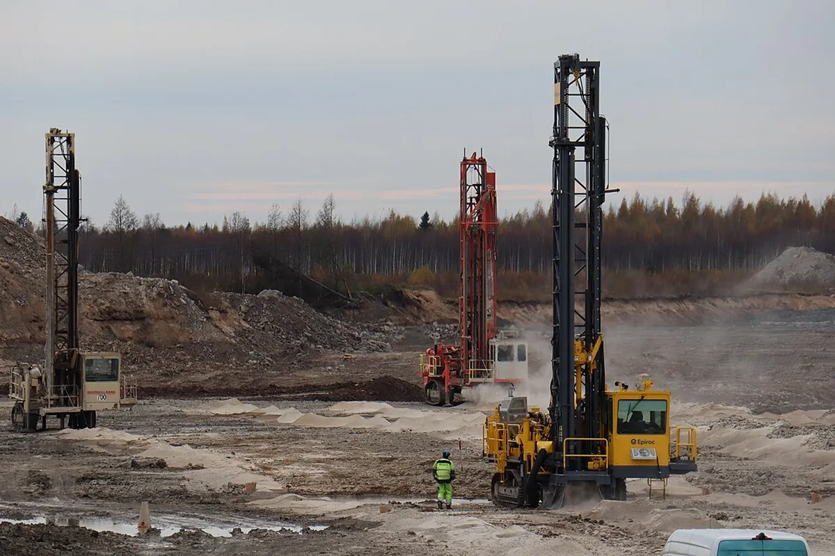 Three crawler blasthole drill rigs drilling overburden in an open-cut mine, an operator in hi-vis standing nearby